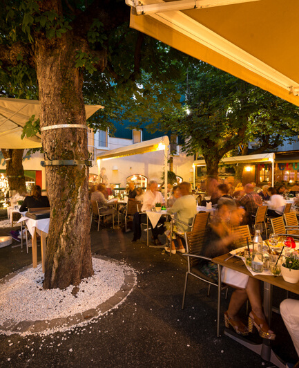 Belebte Terrasse des Hotel Steinerwirt bei Nacht, umgeben von Pflanzen und Gästen.